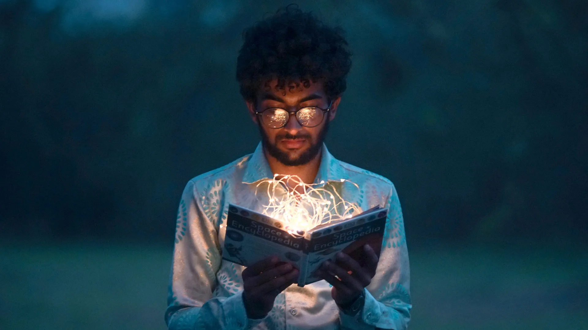A man memorizing a book with lights swirling out of the book